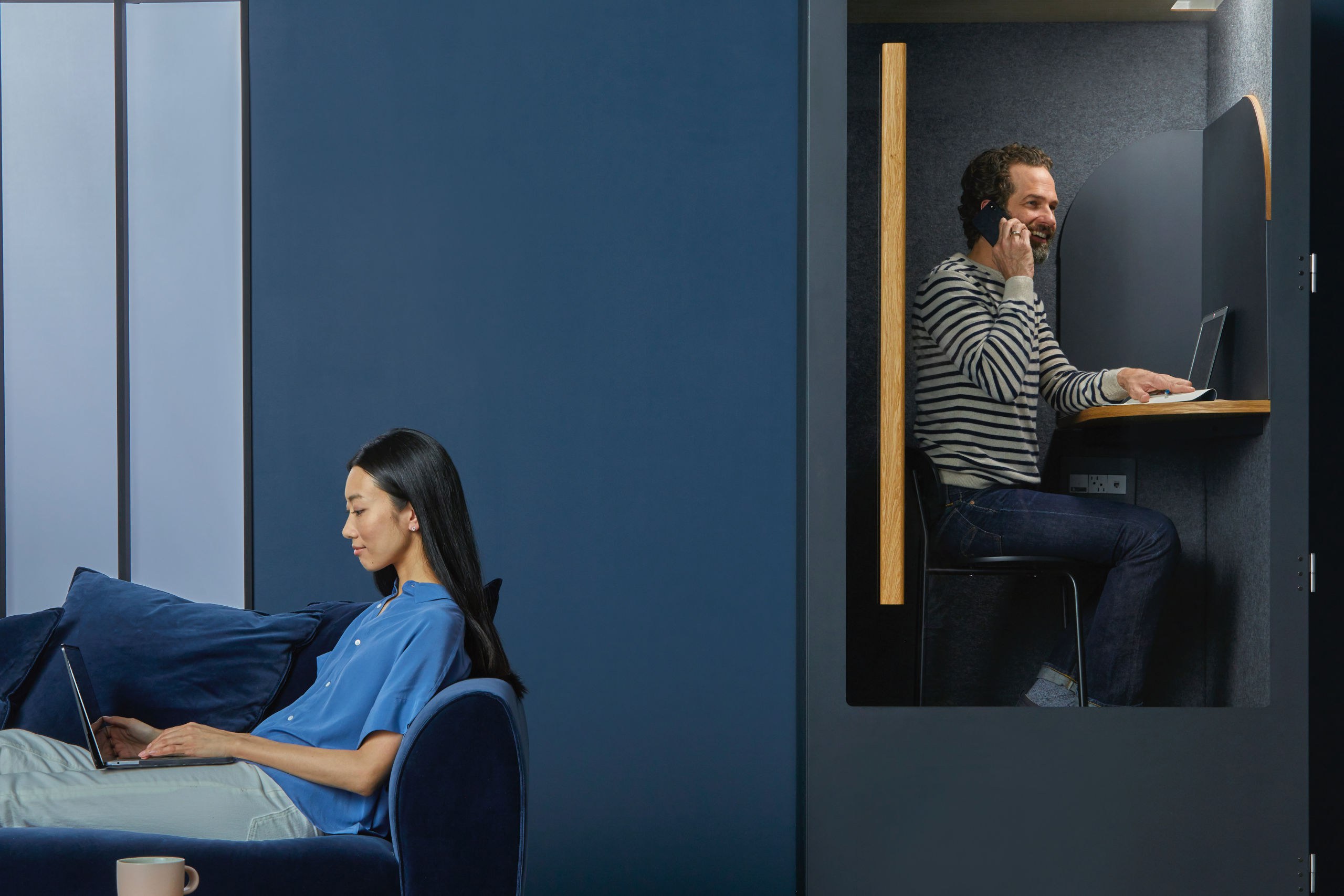 Zwei Personen im blauen Büro, eine Frau am Laptop, ein Mann am Telefon.